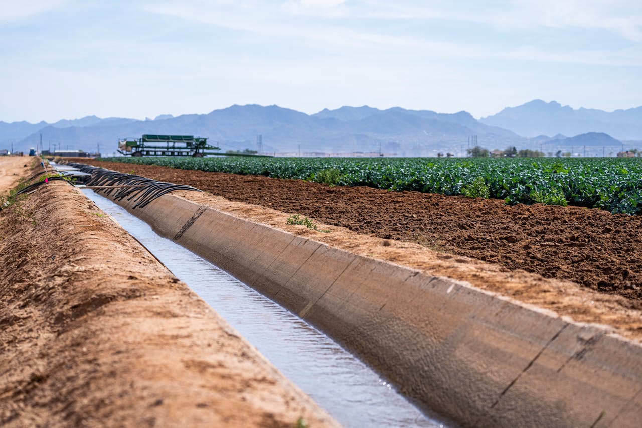 A scenic view of an irrigation canal running through farmland with mountains in the background.